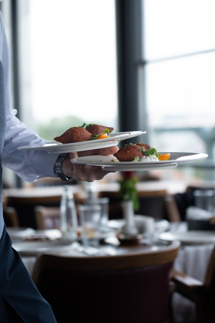A waiter serves gourmet plates in a fine dining setting with blurred background.
