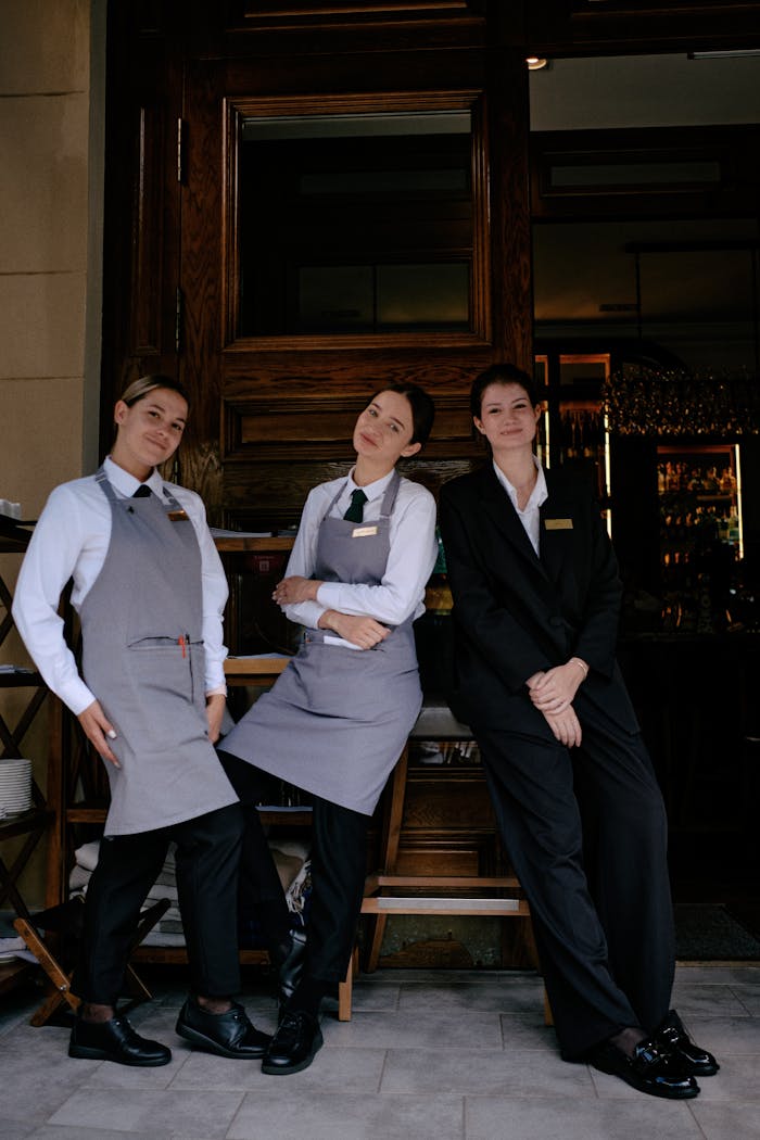 Three restaurant staff members in formal uniforms posing cheerfully in front of a restaurant.