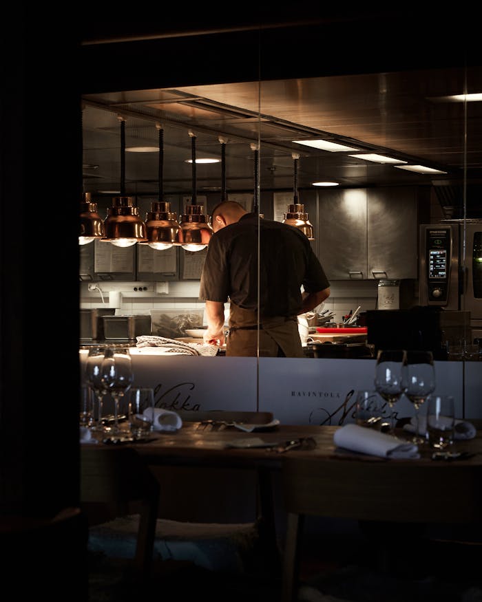 A chef preparing dishes in a stylish restaurant kitchen with dim lighting.